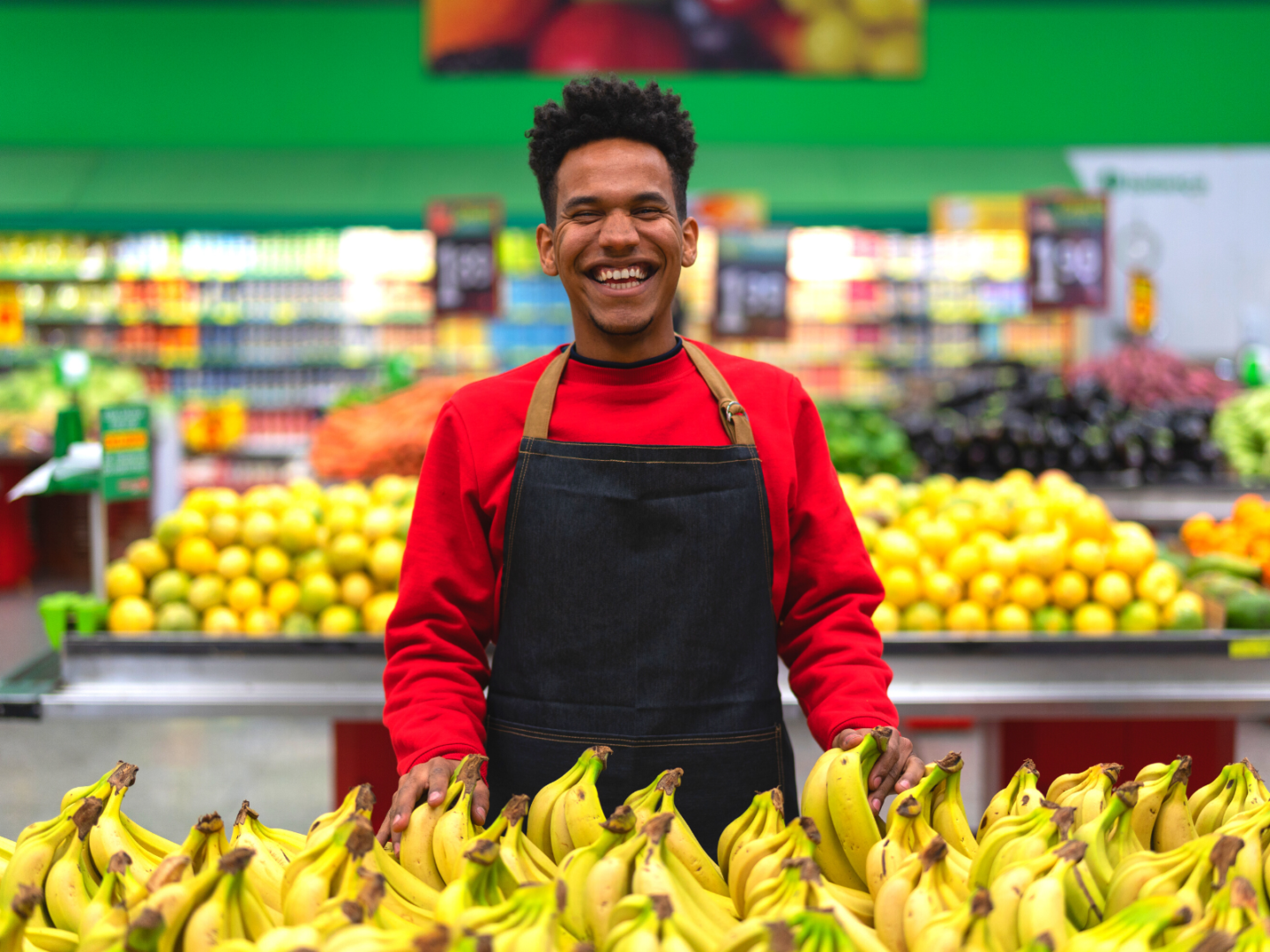 A man wearing an apron in the fruit section of the grocery shop